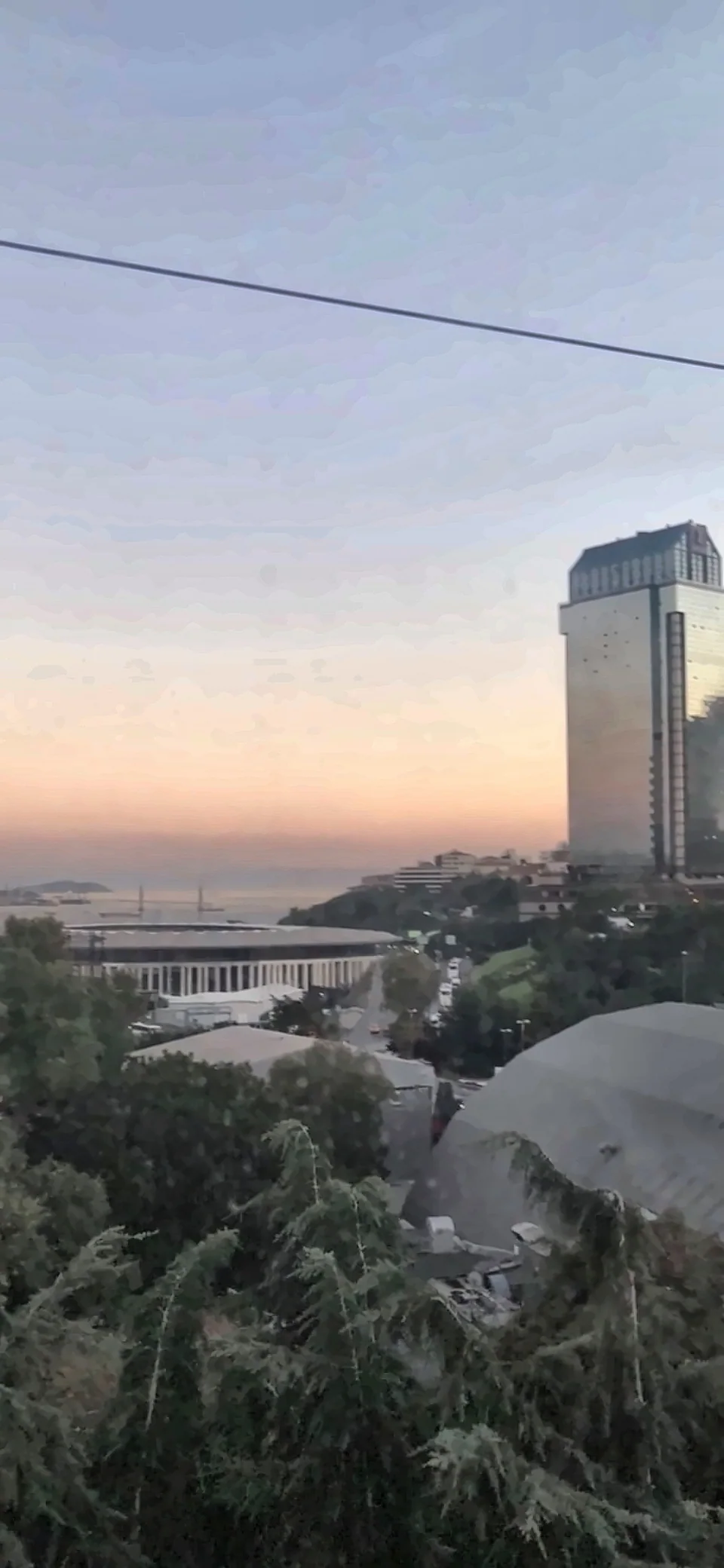 Gün batımı renklerinde kıyı şeridi, yüksek bir bina ve uzakta deniz.