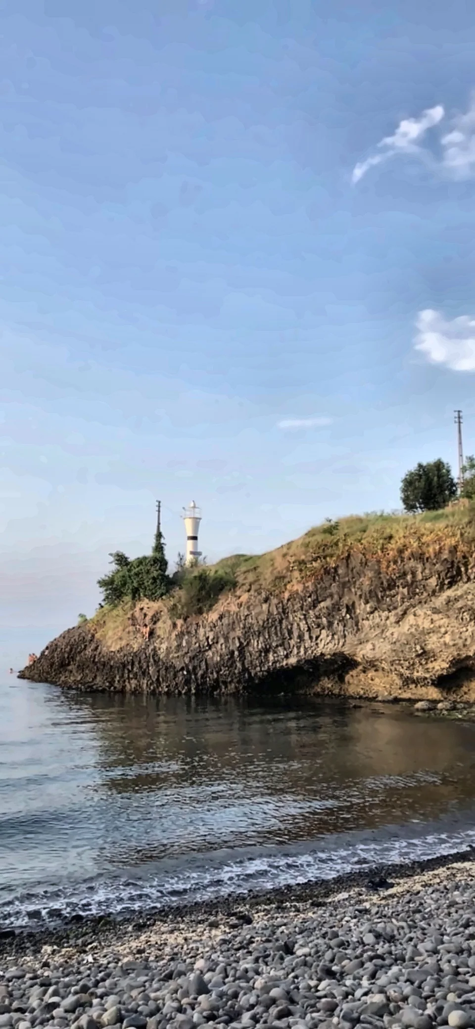 Kayalık bir burun üzerinde küçük bir deniz feneri; önde çakıllı sahil.